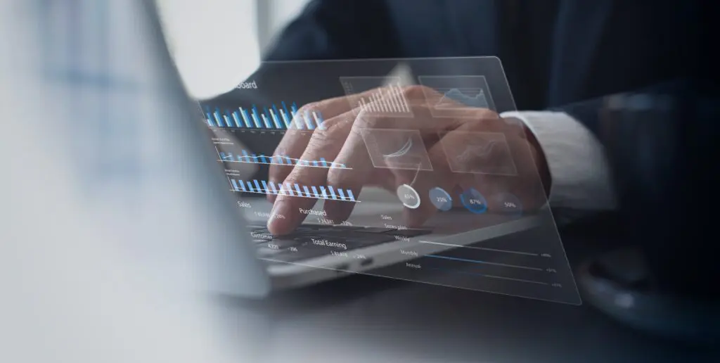 A close-up of a person typing on a laptop keyboard with an overlay of futuristic digital data visualizations, including bar charts, line graphs, and percentage indicators.